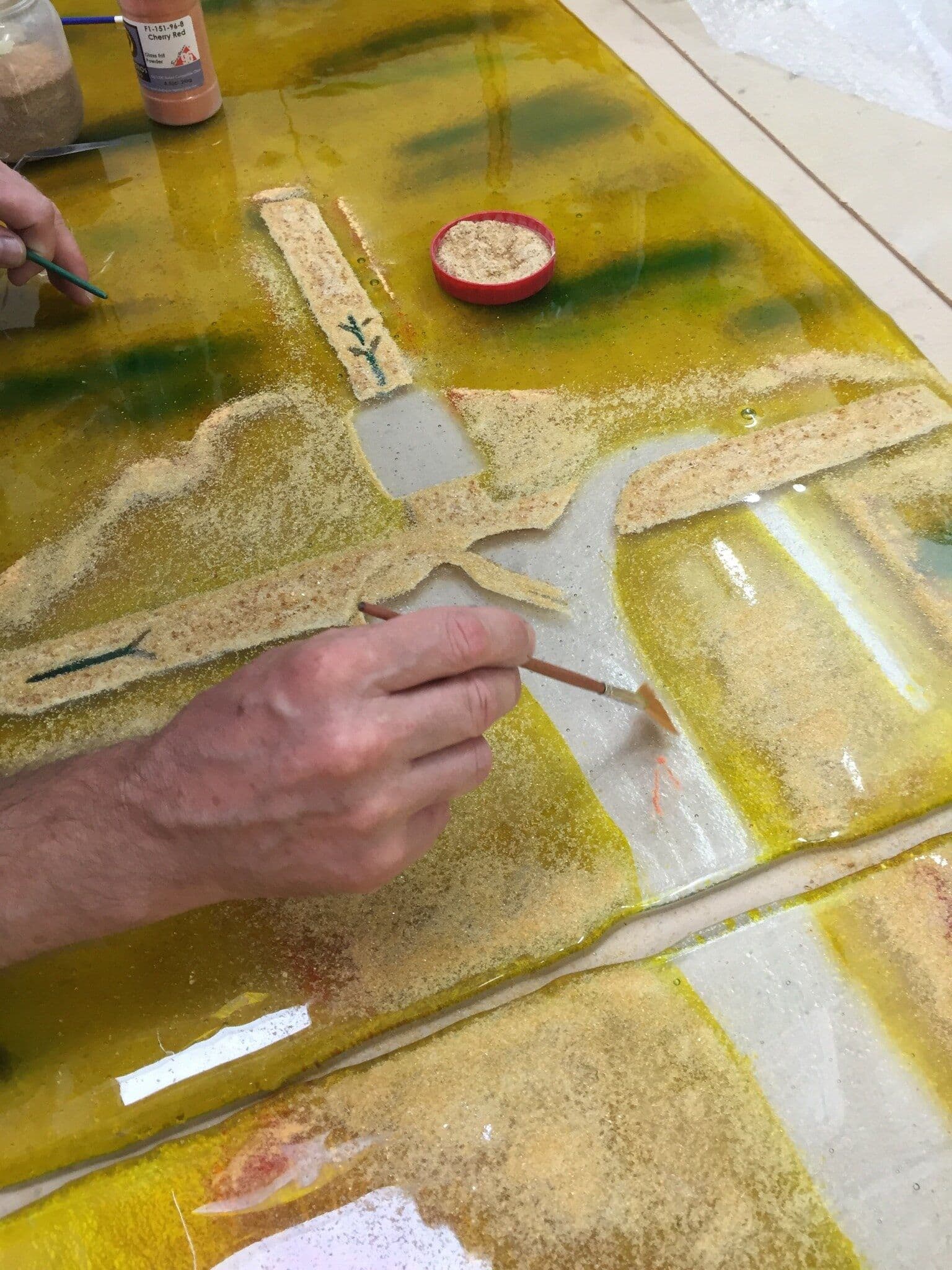 A hand applying glass material around the crucifixion figure on the chapel window panel