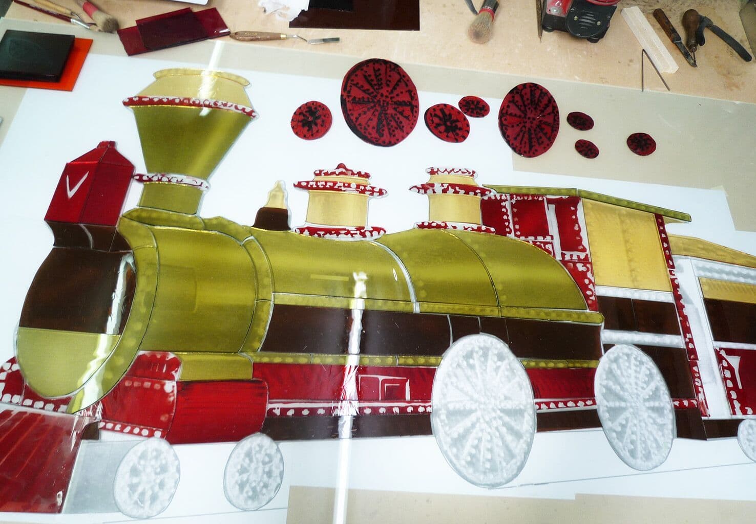 The illuminated train being assembled in coloured glass on a studio workbench