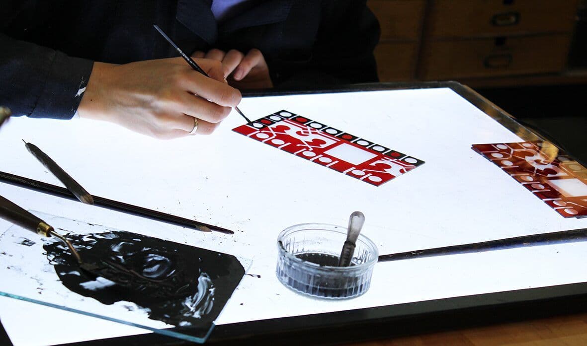 Detailed red and blue glass pieces being hand-painted on a light table