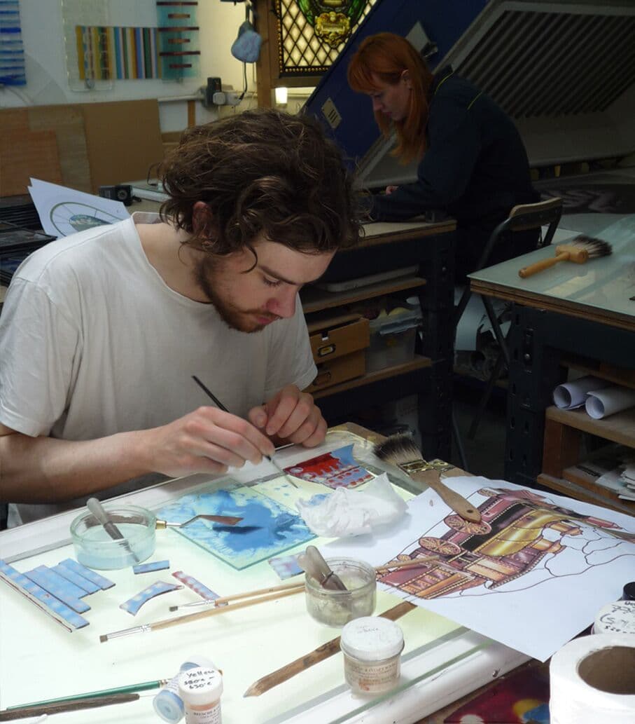 A member of the studio team painting detailed glass pieces for the library windows