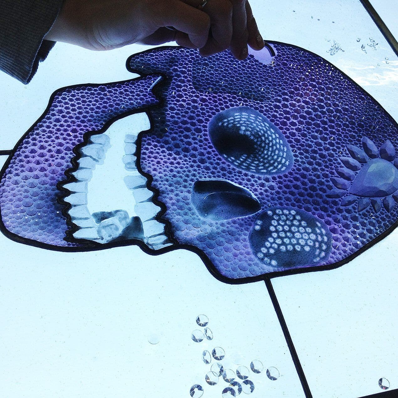 Close view of work progressing across a purple skull panel on a light table